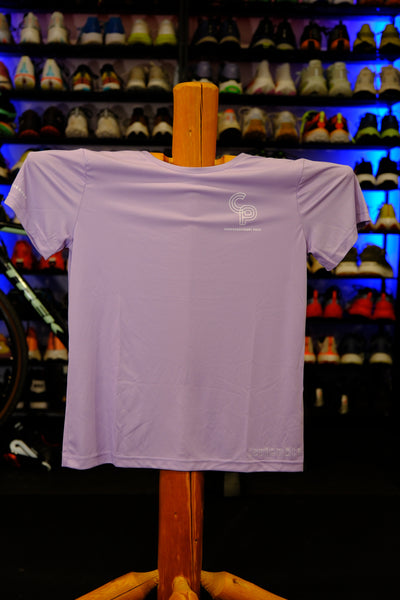 Lavender t-shirt with a logo on a wooden hanger against a colorful stained glass window background